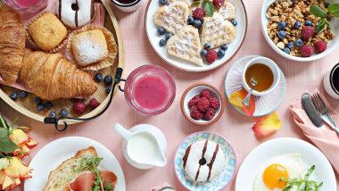 Pink Table filled wit breakfast items like coffee, pastries, eggs and more