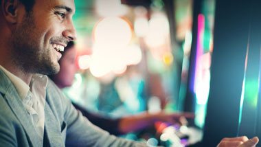 man playing slot, person faded in background