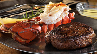 filet and lobster tail with lemon on a black plate