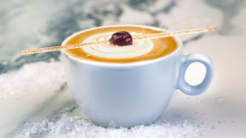 A latte sitting in fake snow with a cherry in the middle of the cup