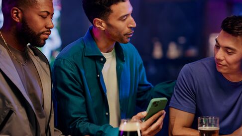 Three men watching sports with beer and one has there phone out like he is placing bets 
